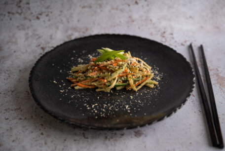 Vegetarian kani salad made with hearts of palm marinated in dill, lemon juice, and nori flakes, served with julienned carrots and cucumbers, topped with sesame seeds and spring onions.